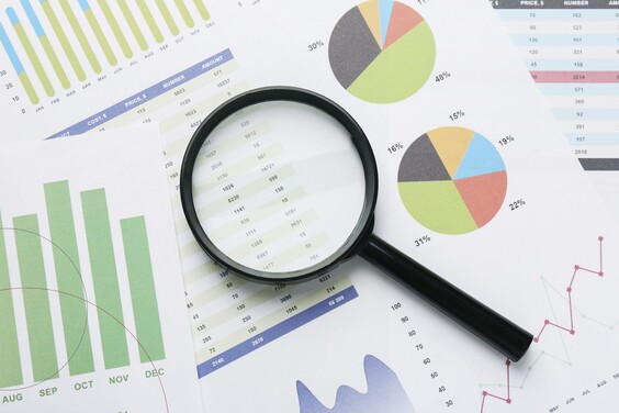 Eine Lupe liegt auf verschiedenen Unterlagen, die Diagramme zeigen.