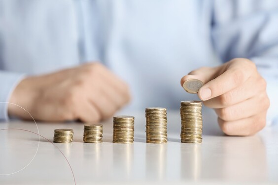 Unterschiedlich hoch gestapelte Geldmünzen stehen auf einem Tisch vor einer Person.