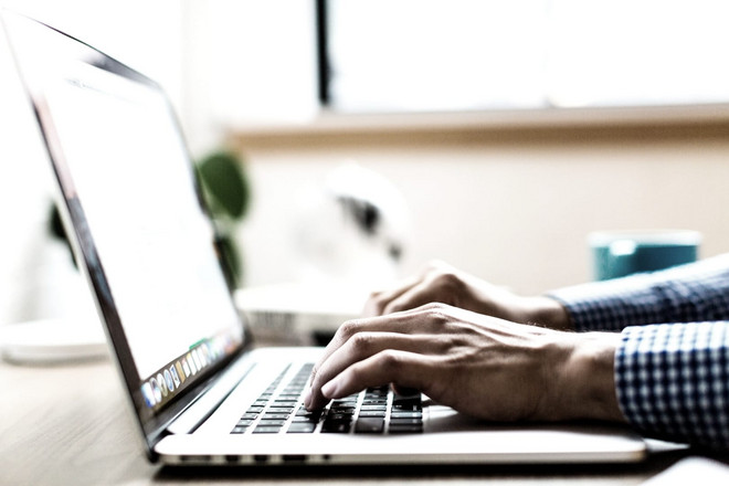 Mann im karierten Hemd schreibt am Laptop