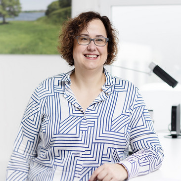 Sandra Gier, Teamleitung von ttp.lohn, steht an ihrem Schreibtisch, im Hintergrund hängt ein Landschaftsbild an der Wand