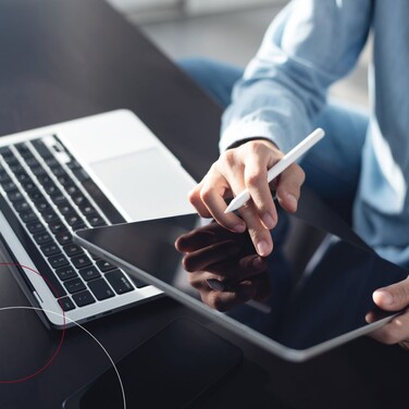 Beispielbild Person im Hemd arbeitet an einem Tablet neben einem Laptop