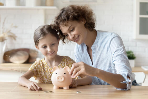 Eine Frau und ein Mädchen sitzen am Küchentisch und befüllen ein rosa Sparschwein mit Geldmünzen.