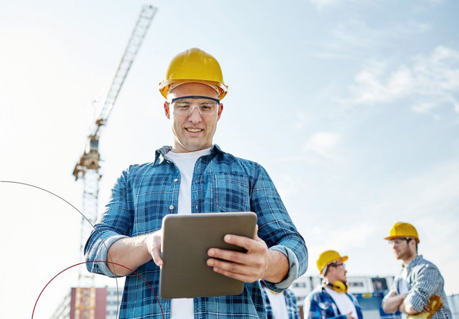 Ein Mann mit Schutzhelm- und brille schaut auf sein Tablet.
