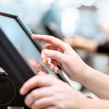 Hände, die etwas in einen Kassenmonitor tippen.