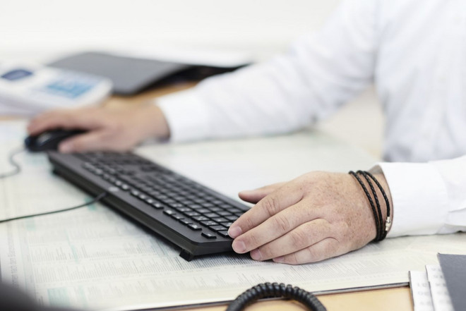 Person, die Maus und Tastatur am Arbeitsplatz benutzt.