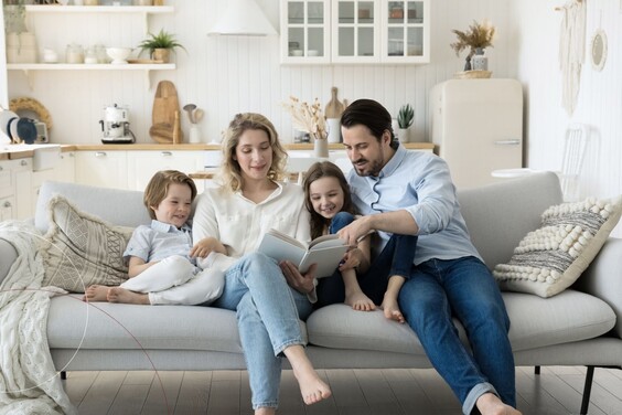Zu sehen ist eine Familie auf einem Sofa, die sich zusammen ein Buch ansehen.
