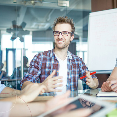 Drei Männer sitzen an einem Tisch und unterhalten sich, im Hintergrund eine Flipchart