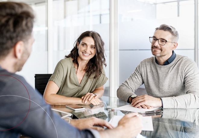 Drei Personen sitzen an einem Tisch im Büro und besprechen sich.
