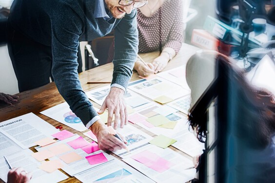 Arbeitsgruppe an einem Tisch, auf dem Papiere und bunte Post-its liegen